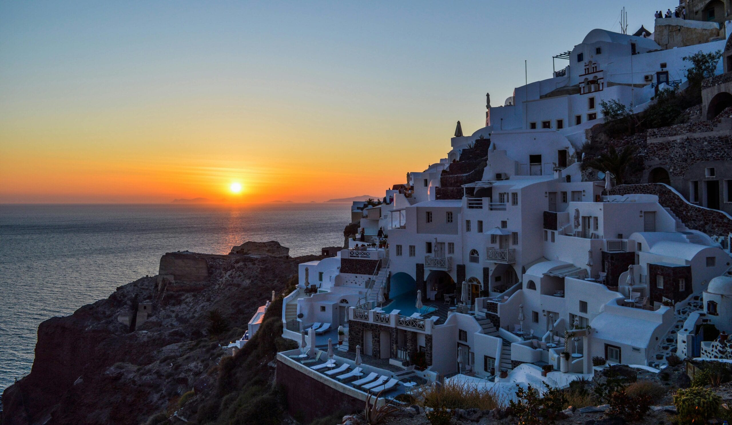 Stunning sunset over the iconic white buildings of Santorini, Greece, with a view of the Aegean Sea.